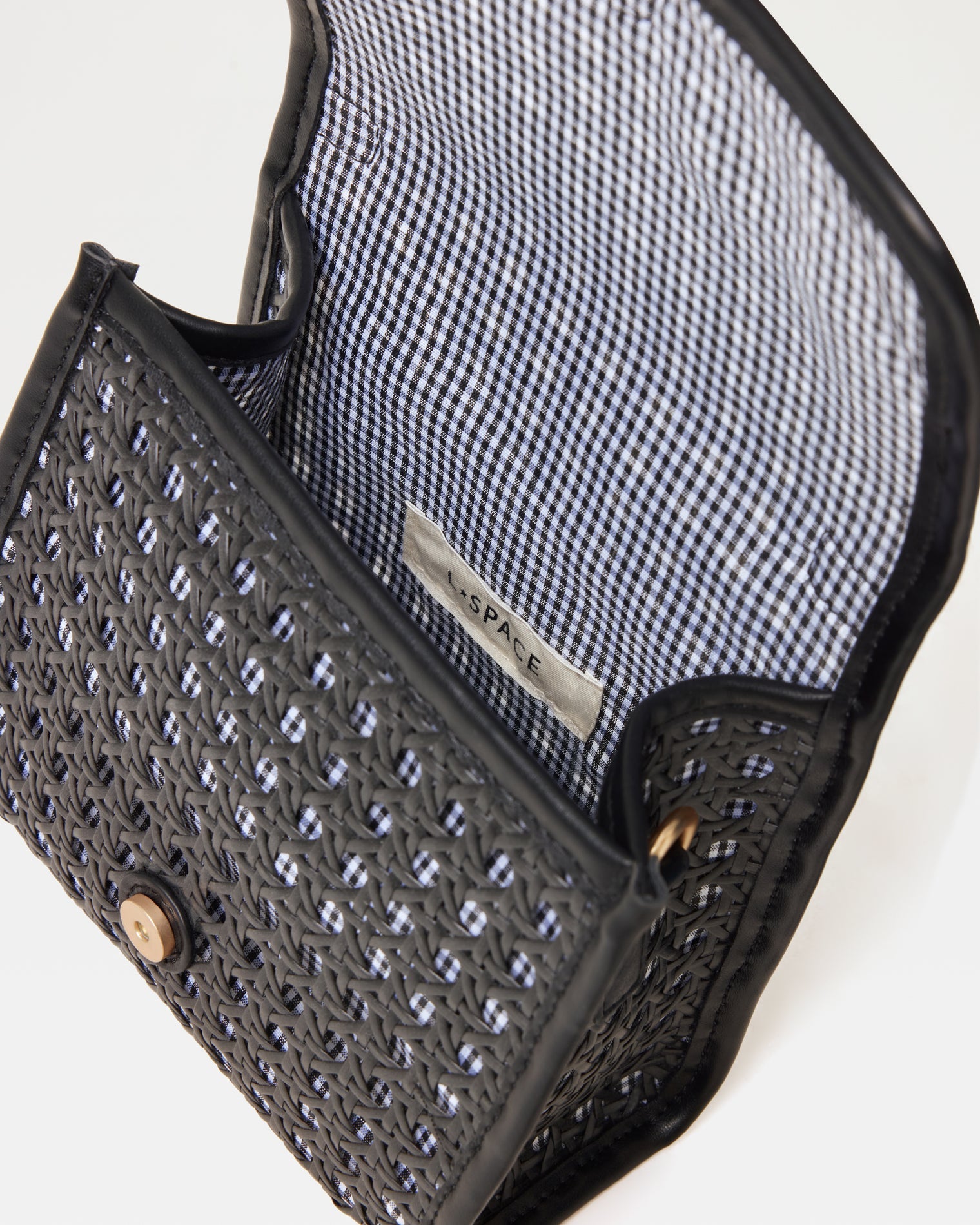 Interior view of the Amelia Bag in black showing the open flap, blue and white gingham lining, LSPACE branding label, and magnetic button closure.