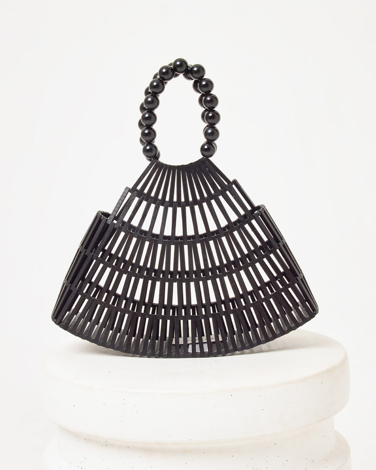 Off-model image of the Starlight Bag in black, a bamboo slat cage-style structured bag with a black beaded handle, on a white pedestal.