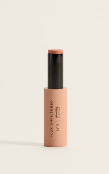 Close-up of Smoothing Lip Tint in Guava held by hand next to model's glossy coral-pink lips, showing creamy tint finish