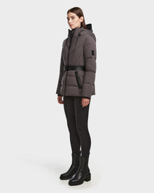 A woman stands slightly sideways against a white background, wearing the Rudsak ENZAH - 8124692 grey belted, hooded down puffer jacket with black leggings and black ankle boots.