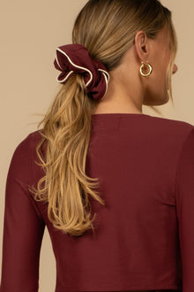 Maroon chunky scrunchie with cream piping worn in blonde hair in a ponytail.