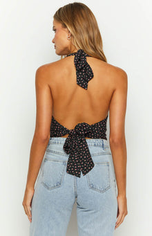 Rear view of a black floral crop top with a halter neck tie and a tie-back closure at the waist