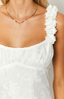 Close-up of the white mini dress showing the textured fabric, gathered bust, and 3D floral shoulder strap