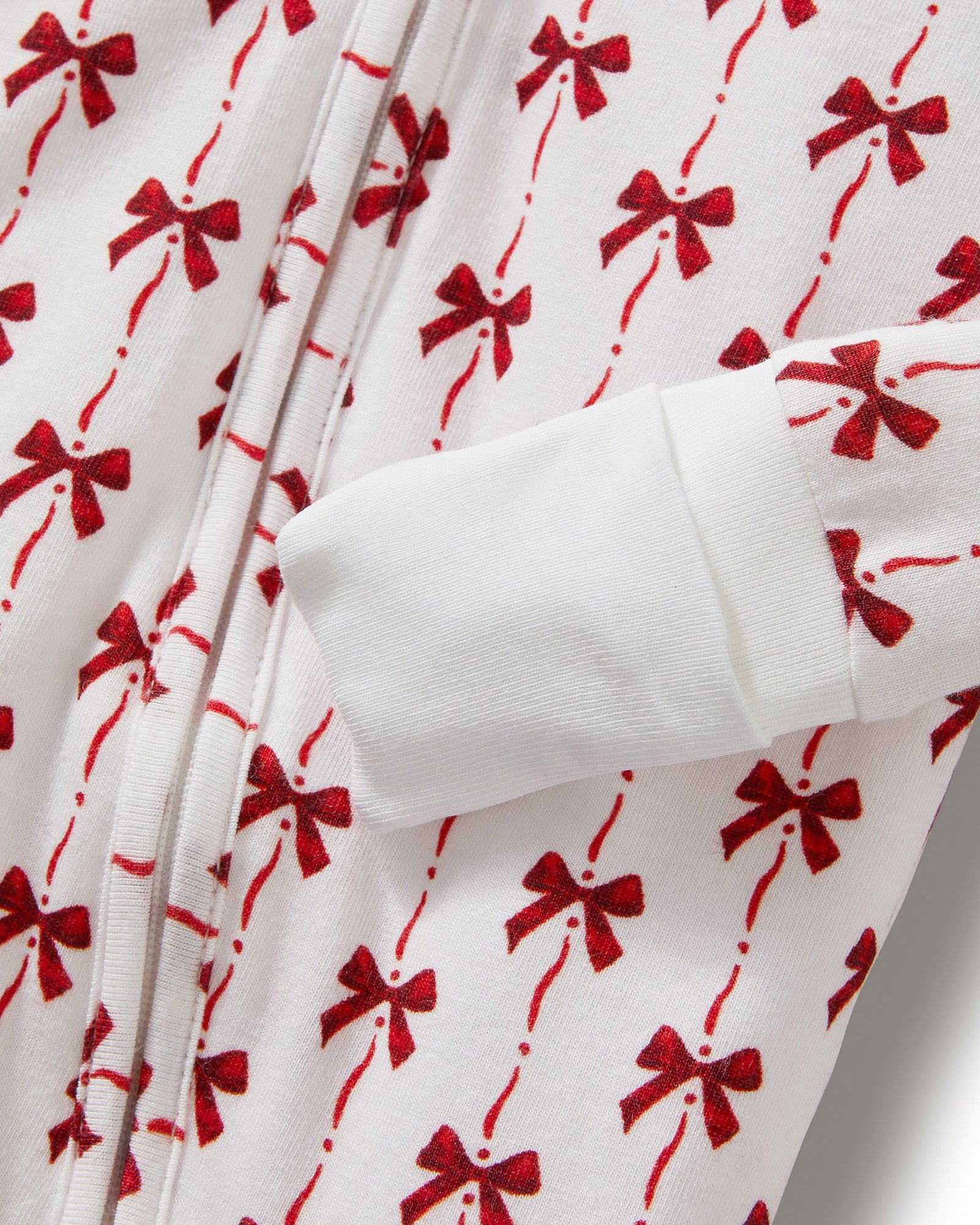 The Baby's Pima Peekaboo Romper in Blissful Bows is a white long-sleeve onesie with cuffs, adorned with festive red bows and a convenient back zipper.