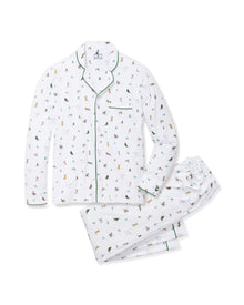 A person smiles in Petite Plumes Mens Pima Pajama Set in Jingle Paws, featuring colorful animal designs on soft Peruvian Pima cotton with green piping and a chest pocket against a plain, light background, enhancing their cheerful appearance.