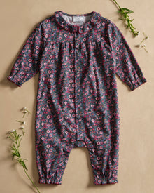 Baby's Twill Madeline Romper in Fleurs de Saison features long sleeves, a dark base with pink and purple floral print, front snap closures, a rounded collar, and gathered cuffs at wrists and ankles.