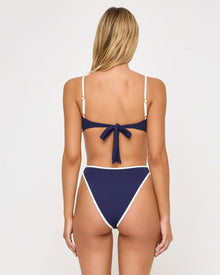 back view of woman wearing a white and navy bikini against a plain background