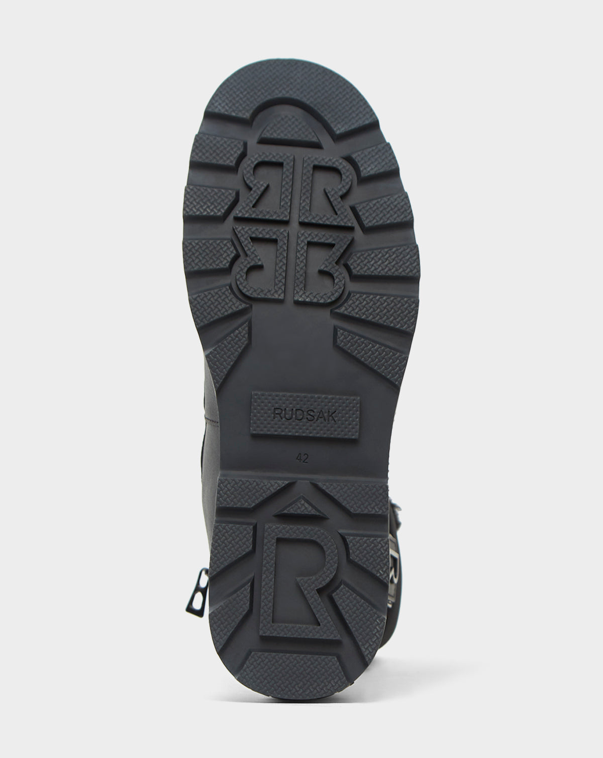The image shows the sole of a black Rudsak LEX - 8222501 boot with the logo and size 42 stamped on it. Its tread pattern features raised R designs and deep grooves, providing reliable traction for waterproof winter wear.