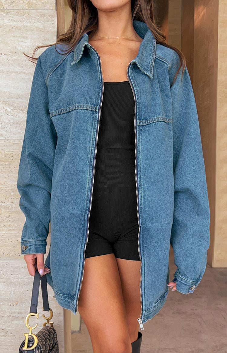 Detail shot of the silver front zipper closure, pointed collar, and orange topstitching on a blue denim jacket