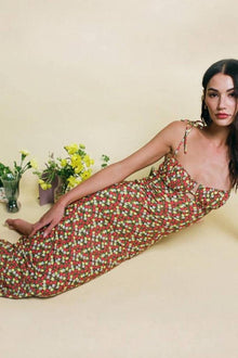 Long slip dress with red, white, and green floral print, thin adjustable straps, worn on cream background.