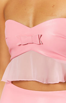 Close-up of the pink faux leather bow detail on the sweetheart neckline of a strapless crop top with a sheer peplum