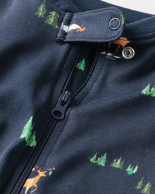 Close-up of Petite Plumes Babys Pima Romper in Arctic Antics, a dark fabric with a zipper and snap button, adorned with small, colorful prints of trees and animals like foxes and bears in a whimsical forest-themed pattern.