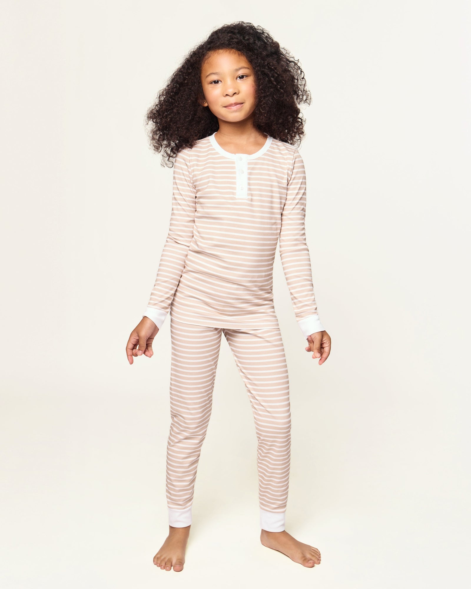 Kid's Pima Snug Fit Pajama Set in Camel Stripe features a beige and white striped long-sleeve top with white cuffs and button placket, plus matching pants with white ankle cuffs.