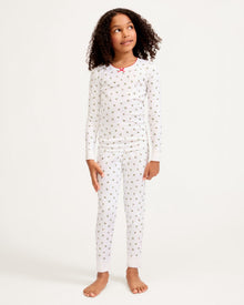 Kid's Pima Snug Fit Pajama Set in Mistletoe Moments: a two-piece white pajama set for children with a long-sleeve top, pants, green and red holly pattern, red scalloped neckline, and a red bow at the collar.