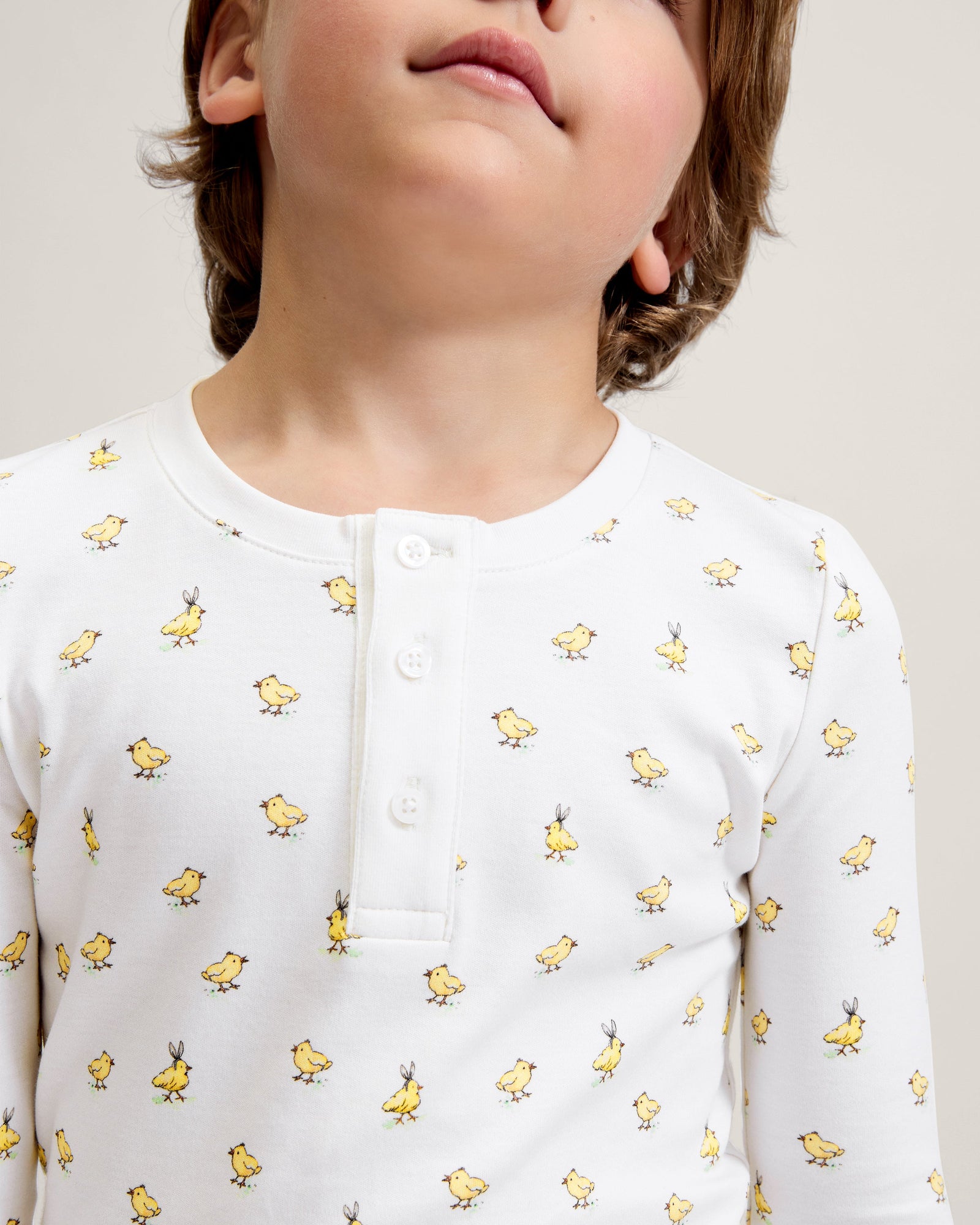 A young child with light brown hair stands barefoot on a plain background, wearing the Kid's Pima Snug Fit Pajama Set in Tres Chick and looking slightly to the side.