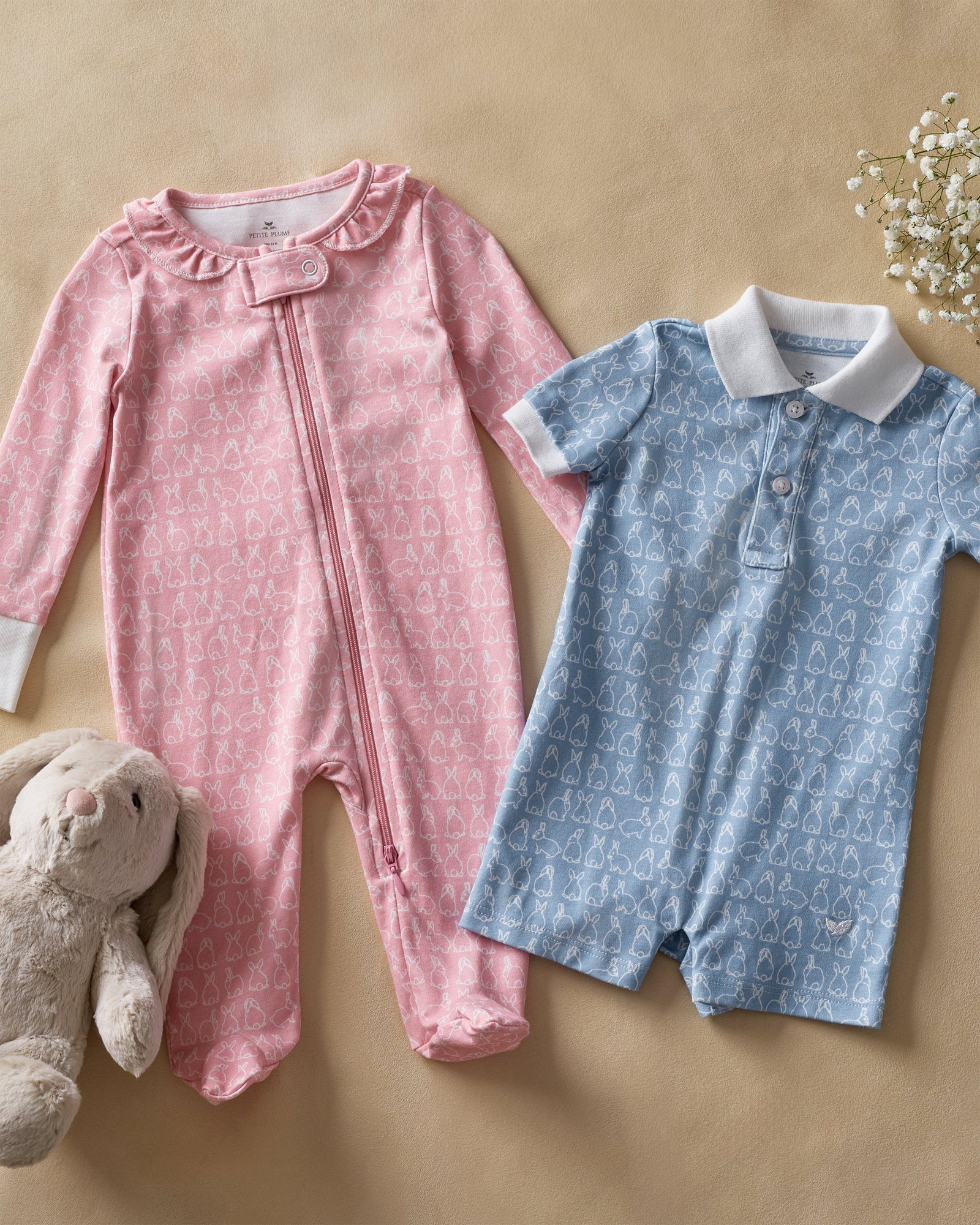 The Baby's Pima Romper in Hoppy Days Pink features long sleeves, white cuffs, a front zipper, a soft white bunny pattern, and a ruffled neckline.