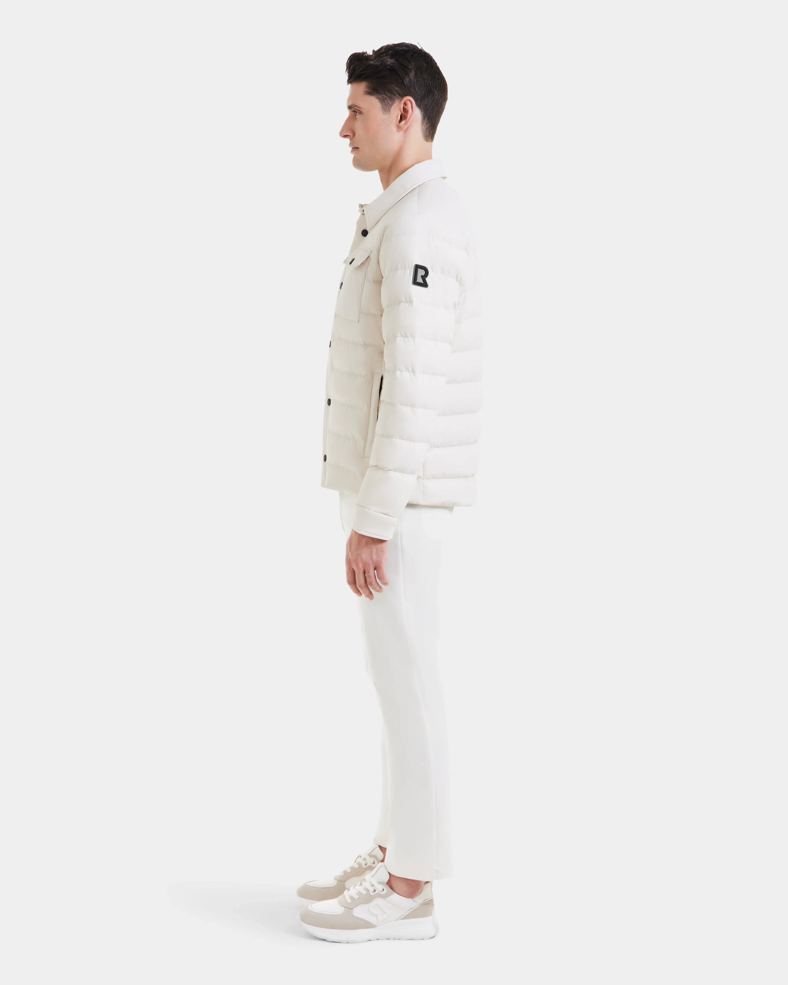 A man in profile wears the Rudsak AZIEL - M124521 Vanilla duck down jacket with white pants and sneakers, posed against a plain white background.