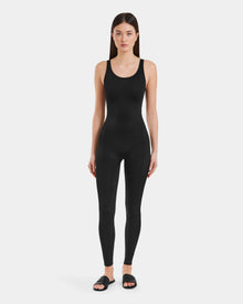 A woman faces forward against a light background, wearing the LAWREN - 8523054 Rudsak Pattern black monogram bodysuit and black slide sandals by Rudsak.