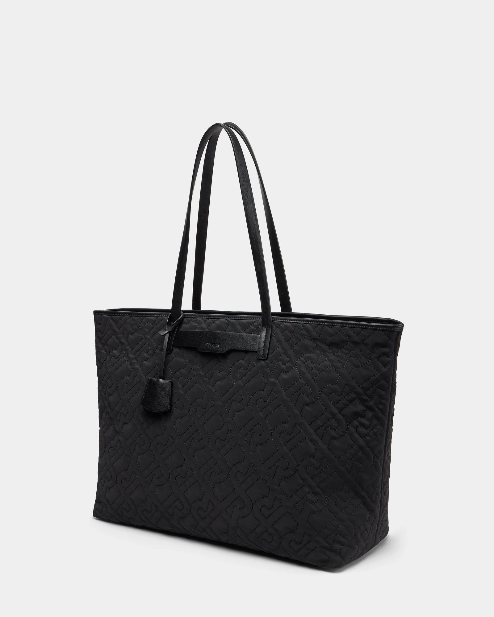 The Rudsak LIVORNO - L325007 Black is a large black luxury tote with a quilted pattern, two long handles, and a small attached pouch near the top. Shown on a plain light gray background.