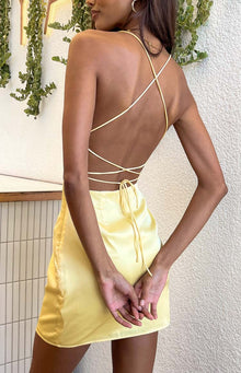 Rear view of a yellow satin mini dress with a low open back and criss-cross spaghetti straps that tie at the lower back