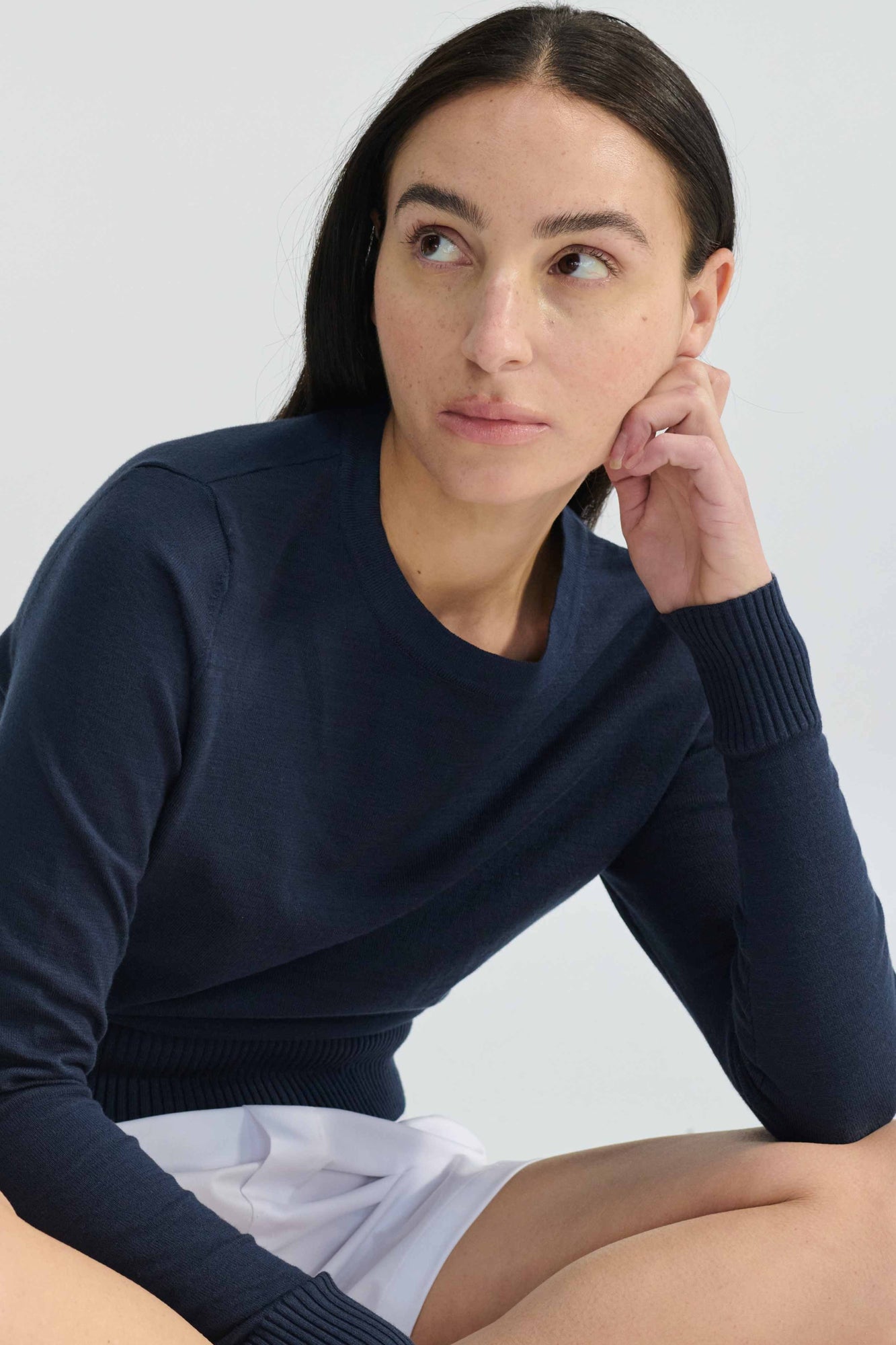 Woman wearing a navy blue sweater and white shorts against a light background