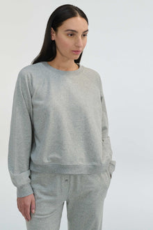 Woman wearing a gray sweatshirt and pants against a white background