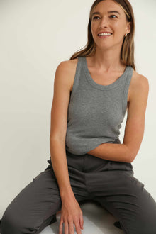 Woman wearing a gray sleeveless top and pants sitting on a white surface.