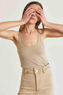 Woman wearing a beige tank top and pants against a plain background