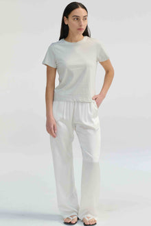 Woman wearing a light grey t-shirt with white pants on a light grey background