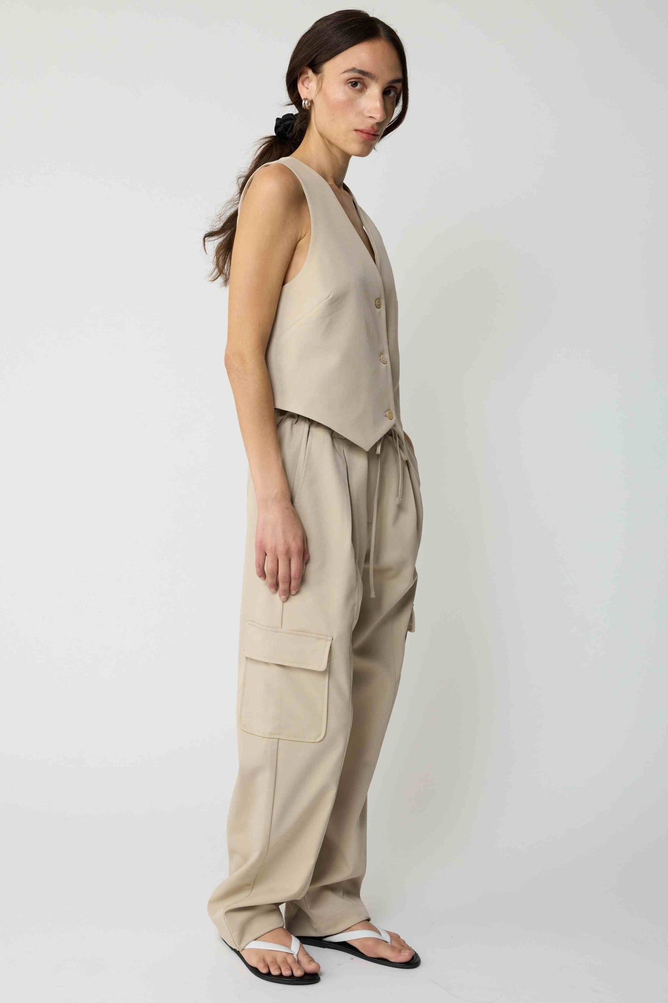 Woman wearing a beige tencel button up vest with beige cargo pants on a light grey background