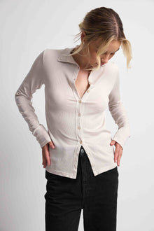 Woman wearing a pink button up top with black bottoms on a light grey background