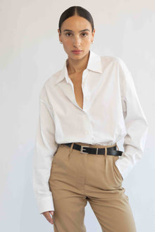 Woman wearing a white shirt and beige pants against a plain background
