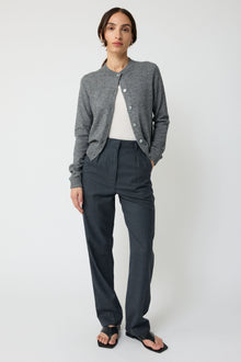 Person wearing a gray cardigan and dark pants on a white background