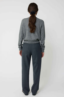 Person wearing a gray sweater and dark gray pants on a white background