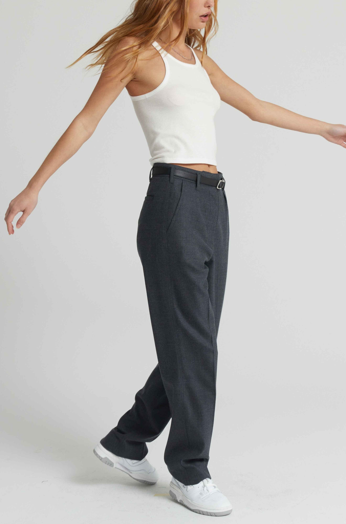 Person wearing a white tank top and dark gray pants on a plain background