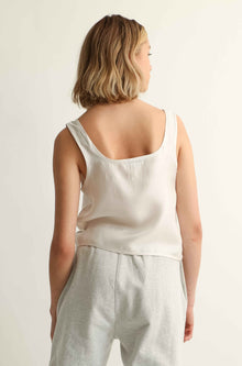 Person wearing a white sleeveless top and light gray pants on a plain background