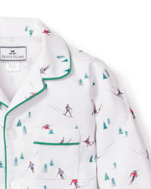 Petite Plumes Kids Flannel Pajama Set in Apres Ski features white flannel adorned with skiers and green trees, green piped trim, and a chest pocket. The collar label assures quality comfort with flame-retardant fabric.
