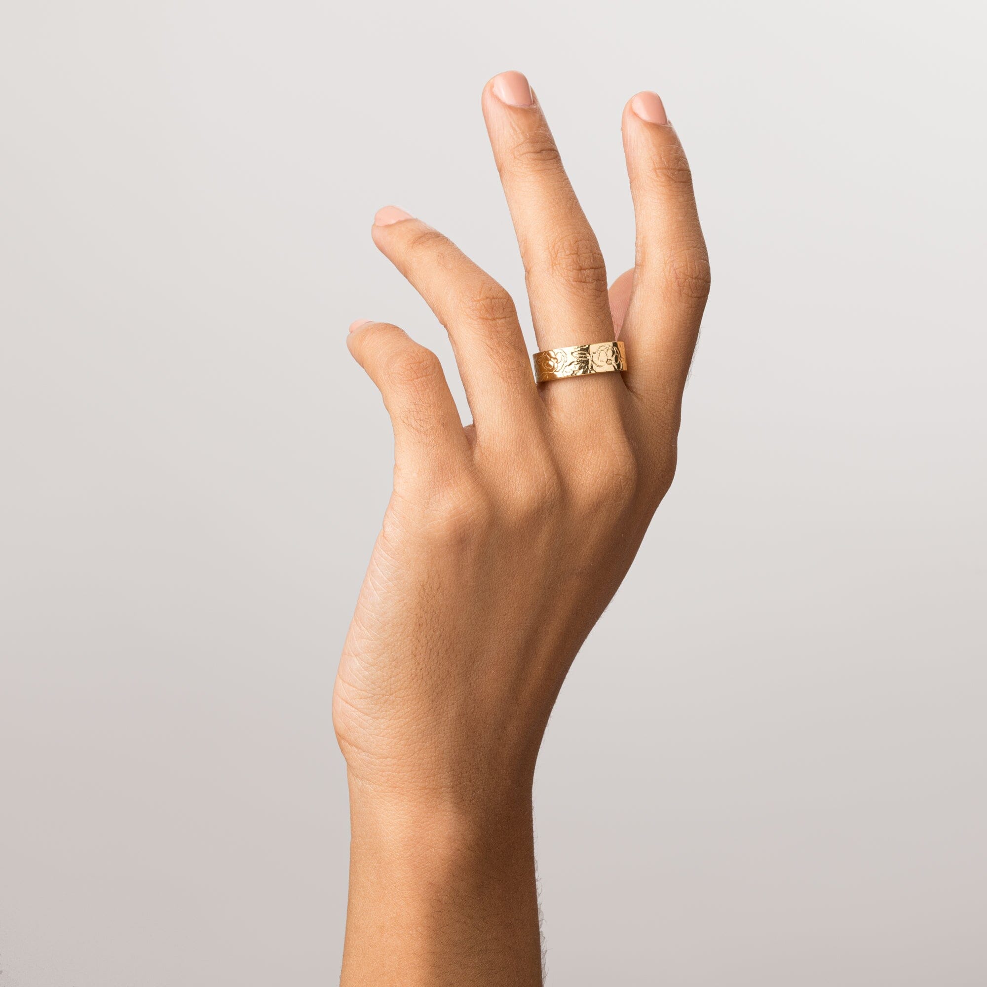 Model Close-up of a woman's hand with fingers gently curled upward, wearing a wide gold ring with an engraved floral design