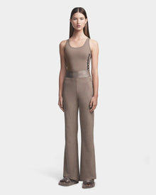A woman faces forward against a white background, wearing the Rudsak SEDONA - 8523541 Cement taupe sleeveless tank top and matching faux suede flare joggers. Fluffy slippers complete her look.