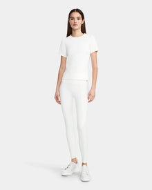 A woman faces forward wearing the Rudsak SUMI - 8524030 Cotton White womens essential tee, paired with white leggings and white sneakers, against a plain light gray background.