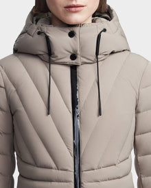 A close-up of a woman in the Rudsak HANNA - 8123562 Cement down jacket. This RDS certified winter coat features black drawstrings, collar buttons, and a front zipper. The womans face is partially visible.
