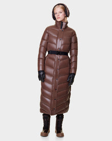 A person wearing the Rudsak ELSIE - L121525 CAOCAO womens maxi down puffer with RDS-certified down, black gloves, lace-up boots, and a knitted hat stands facing forward against a plain light gray background.