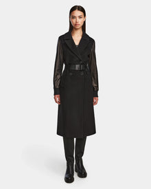 A woman faces forward in the MARYLIN - 8124520 Black by Rudsak, a long black womens wool coat with leather sleeves, worn with black pants and boots against a plain white background.