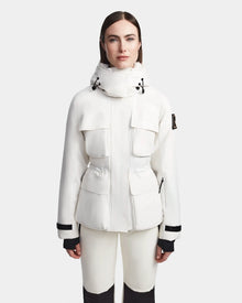 A woman faces forward in a Rudsak LUX - 8123618 Iceland white ski jacket with large front pockets, black trim, and RECCO technology, paired with matching white pants against a plain light background.