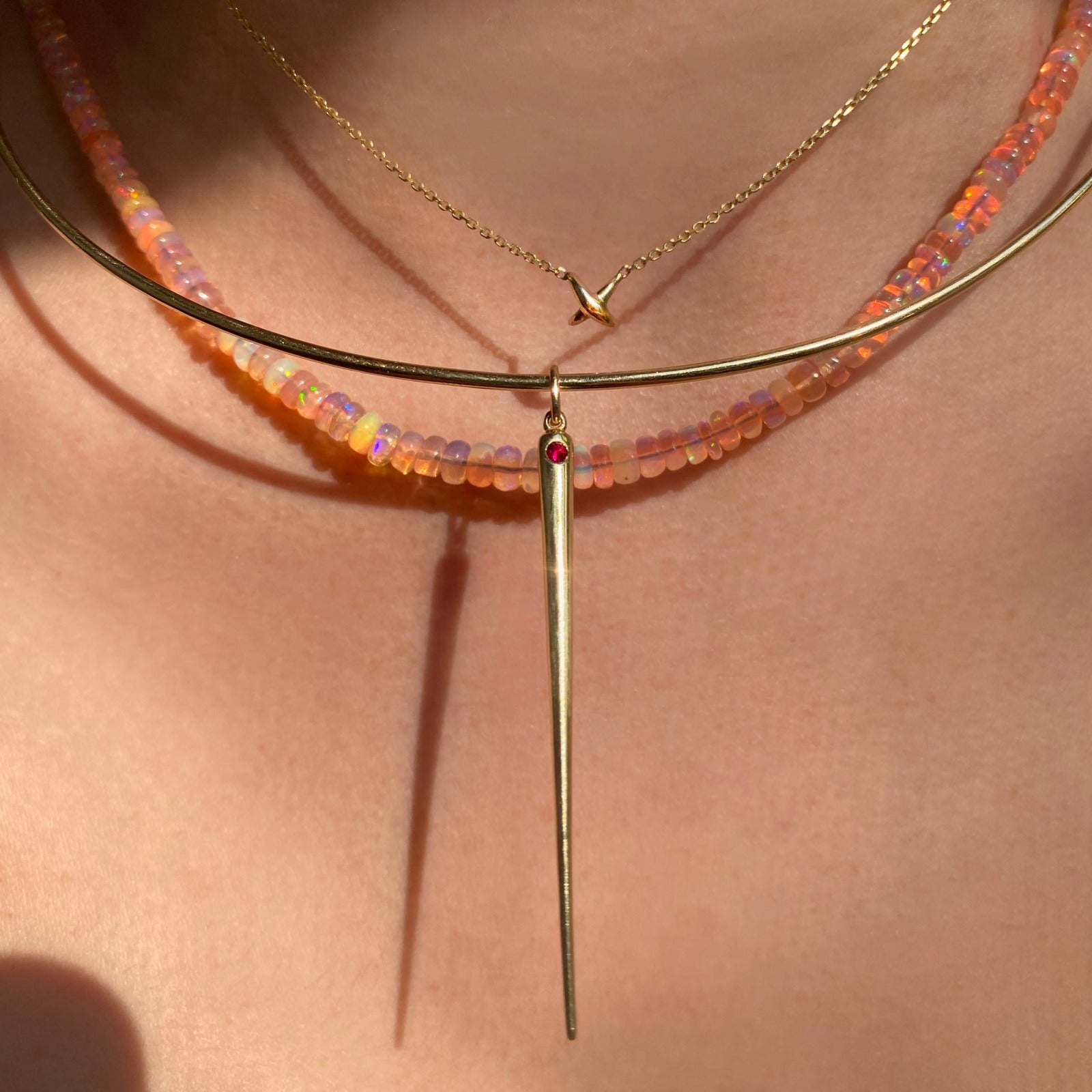14K Recycled Gold Quill Spike Charm with Ruby layered on a gold wire choker styled on a neck with pink opal necklace and gold stitch chain