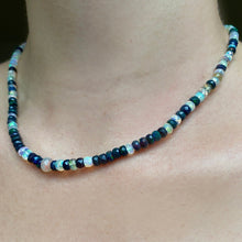 Shimmering beaded necklace made of faceted opals in shades of fiery pastels, grey, teal, and black on a gold linking ovals clasp, styled on a neck