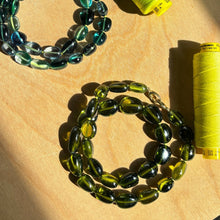 Shimmering beaded nugget bracelets with shades of green, yellow, and olive 
 and blue on a gold lobster clasp on surface.